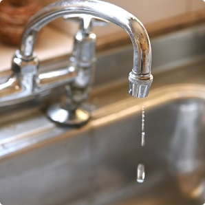 Leaking kitchen faucet dripping into a stainless steel sink.